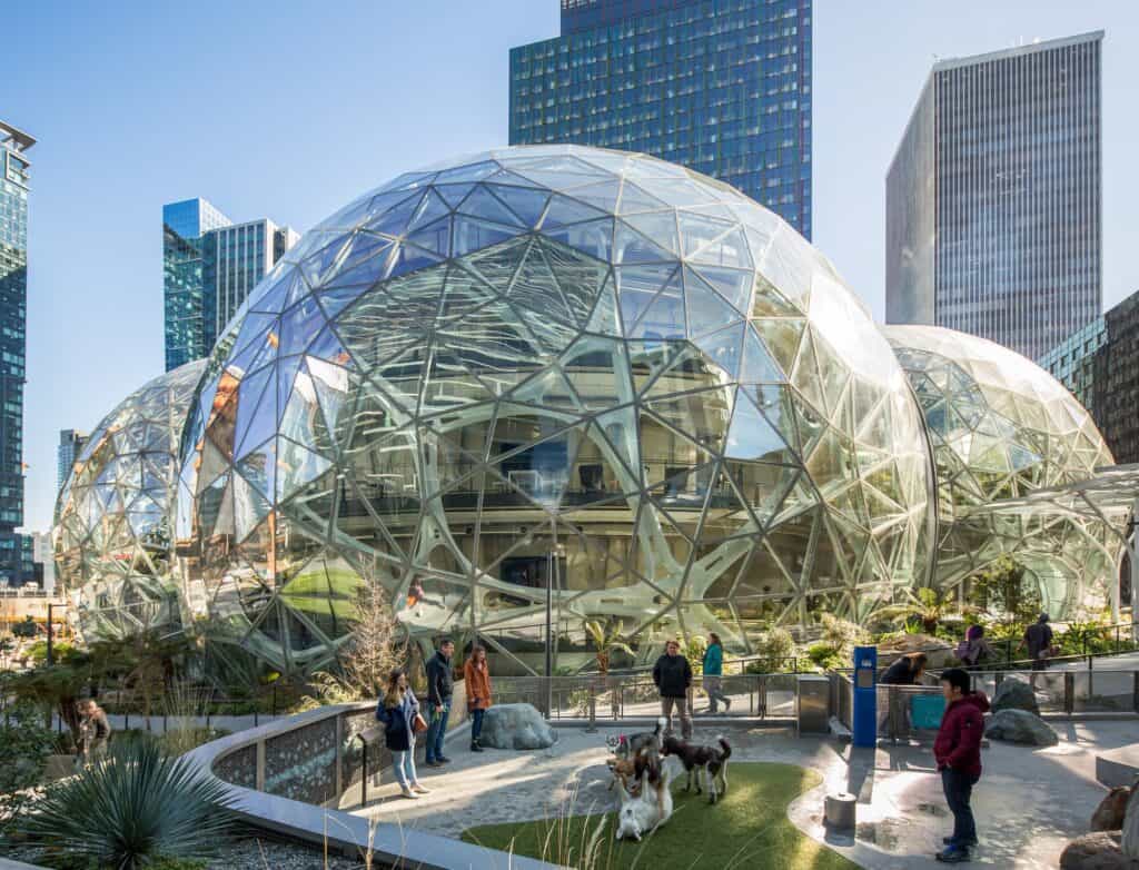 Three interlocking glass domes of the Amazon Spheres beside downtown Seattle towers, a small dog park plaza in front.
