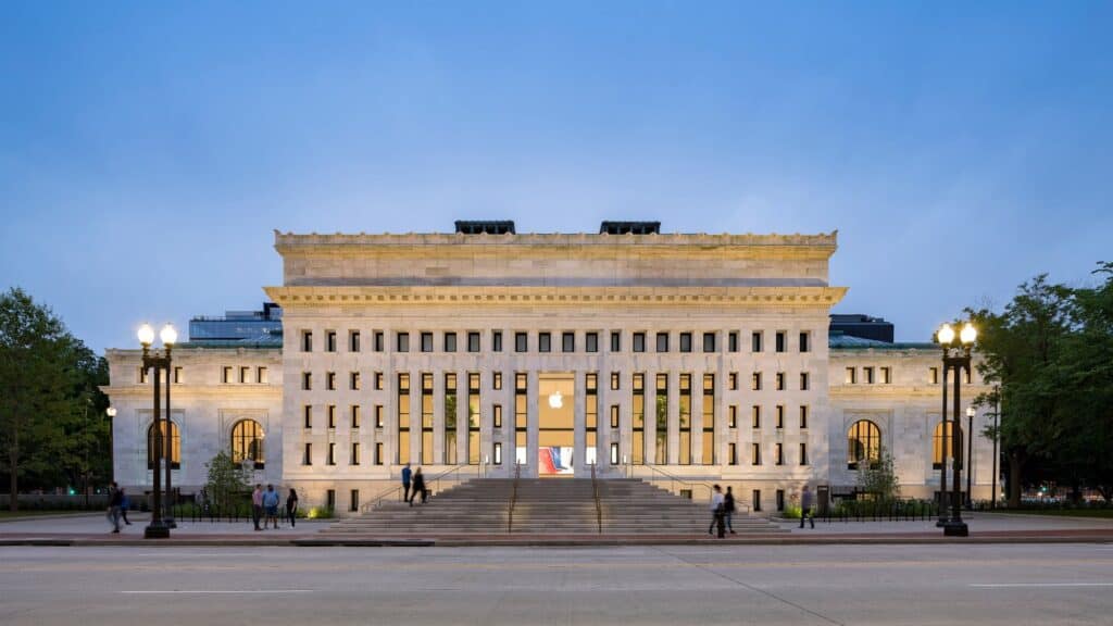 North facade of Apple Carnegie Library at dusk, a rhythm of tall narrow windows above the new grand staircase on Mount Vernon Place, the glowing Apple logo at the entrance and lamp posts either side