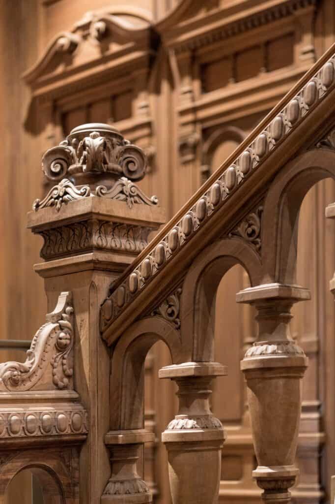Close-up of the restored carved timber escalier d'honneur at Apple Champs-Élysées, a scrolled newel post, beaded handrail and turned balusters against panelled woodwork