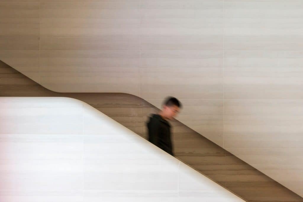 A visitor on one of the twin stone staircases at Apple Regent Street, its smooth curved balustrade carved into the pale sandblasted stone wall