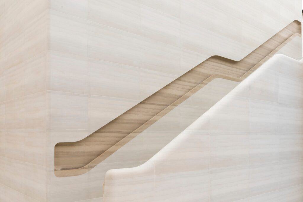 Stone staircase at Apple Regent Street seen side-on, the recessed handrail stepping diagonally past two landings across a wall of pale banded stone