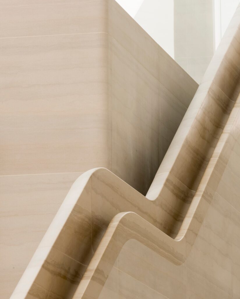 Zigzag stone balustrade of a staircase at Apple Regent Street rising past a landing, its honed curved edge catching soft daylight