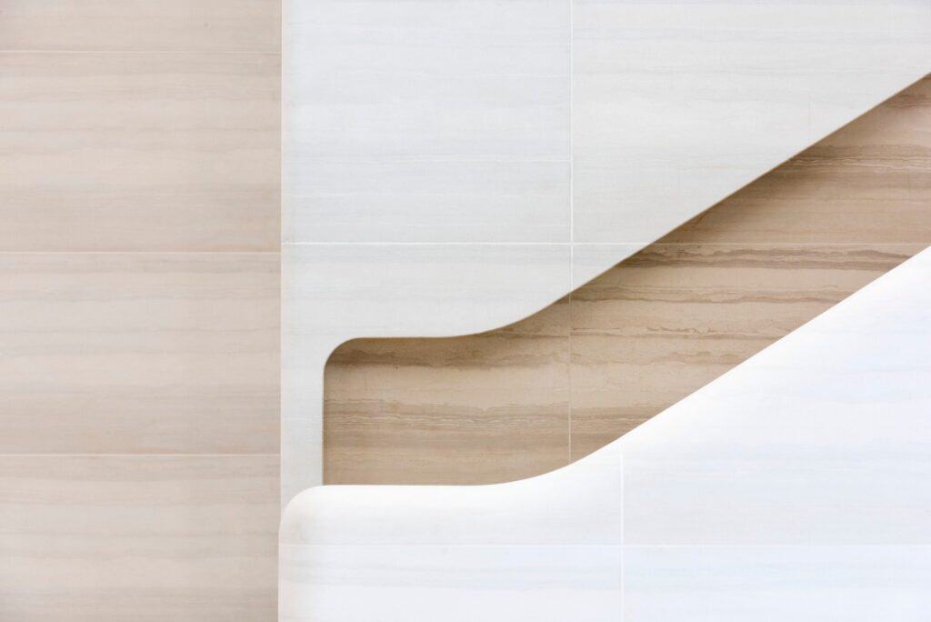 Detail of a stair landing at Apple Regent Street where the carved stone balustrade turns, a warm-toned handrail recess cut into the pale stone wall beside a projecting stone corner