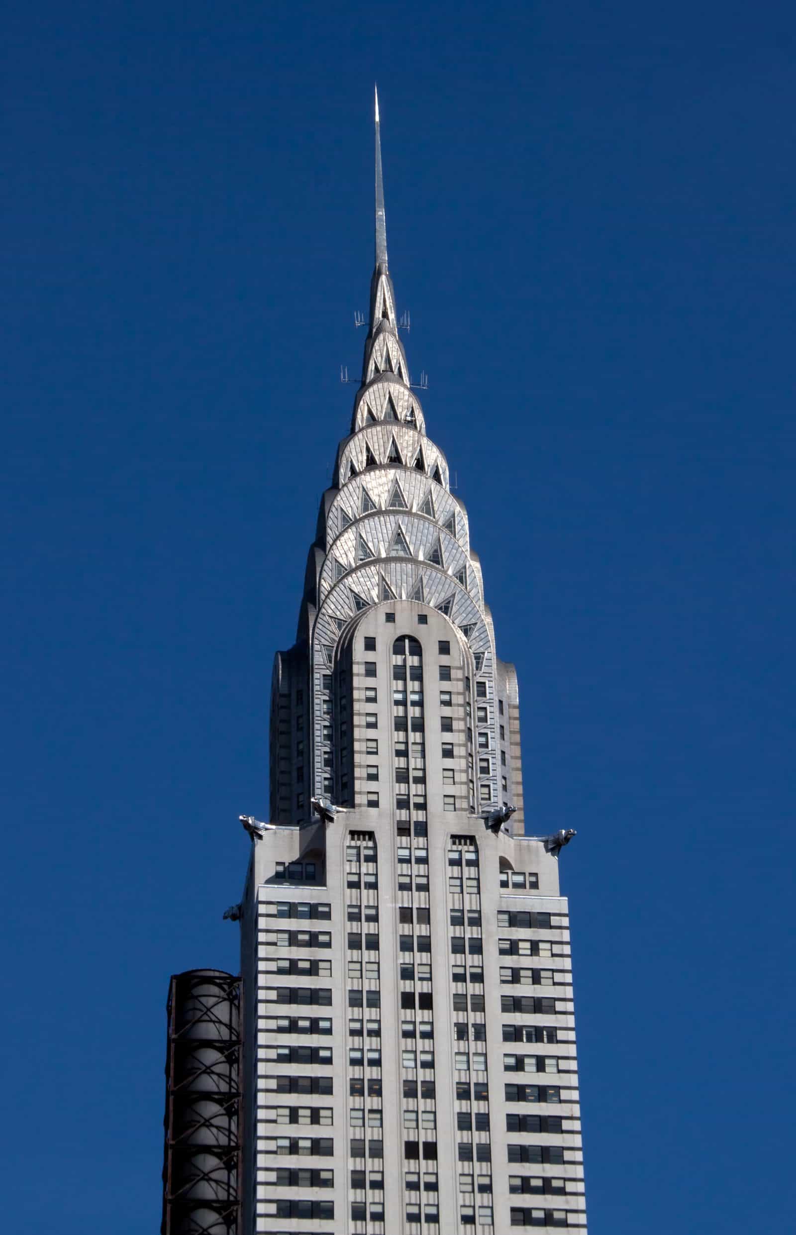 The stainless steel crown of the Chrysler Building in New York, with stacked sunburst arches, triangular windows and a needle spire against a deep blue sky