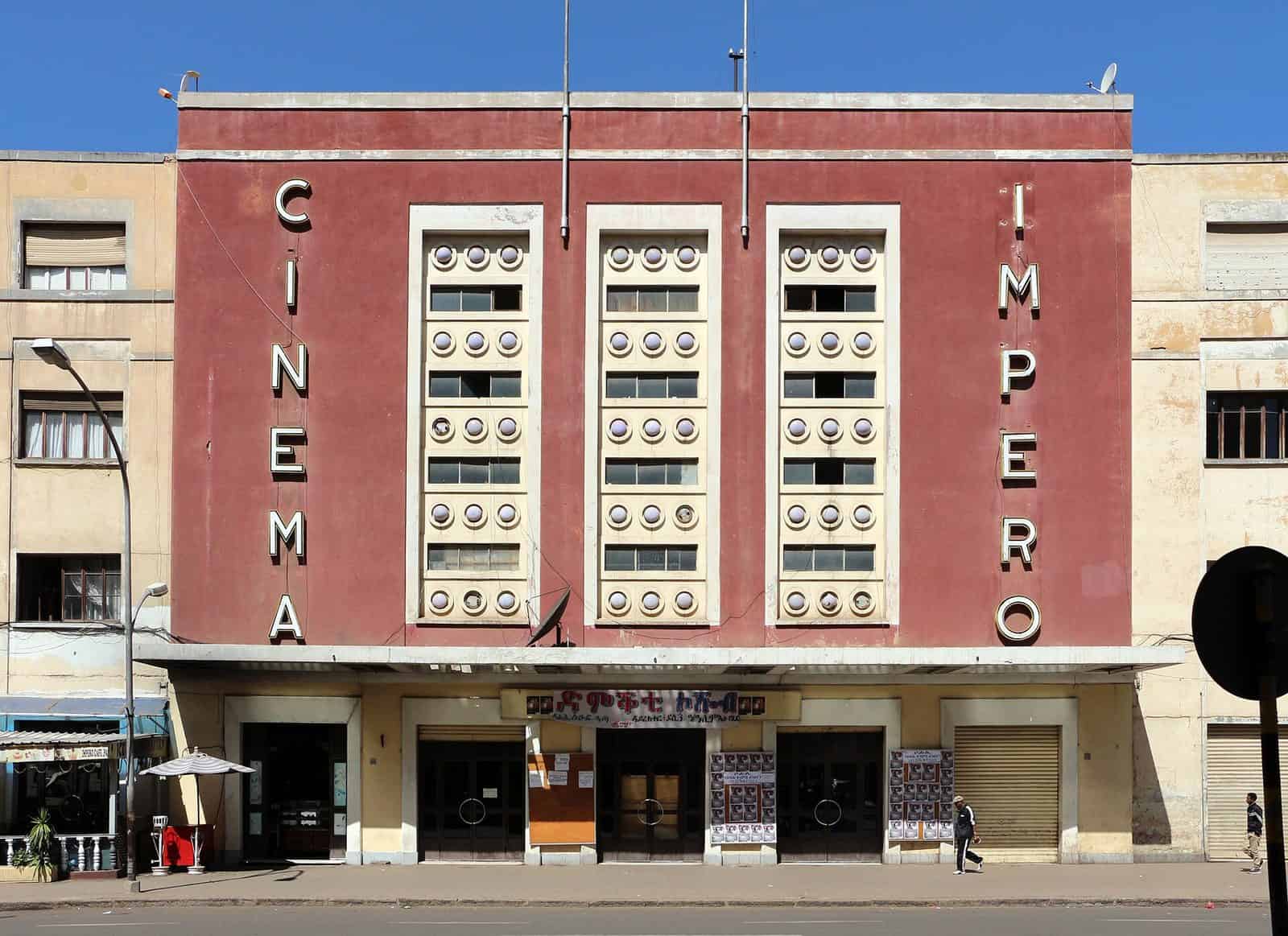 The red facade of Cinema Impero in Asmara, Eritrea, with three cream panels of round lights and the words Cinema and Impero in vertical lettering