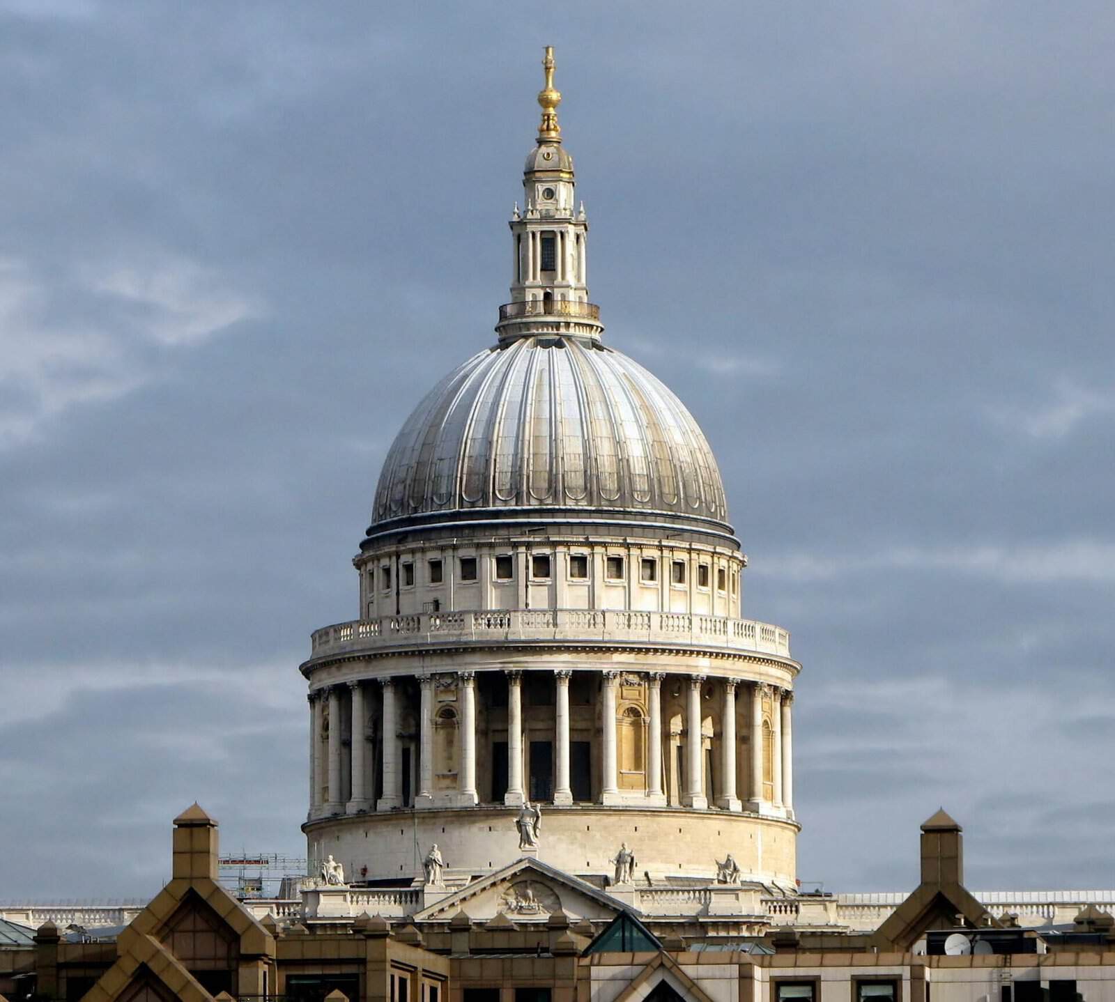 The grey lead dome, colonnaded drum and golden cross of St Paul's Cathedral in London under a cloudy sky