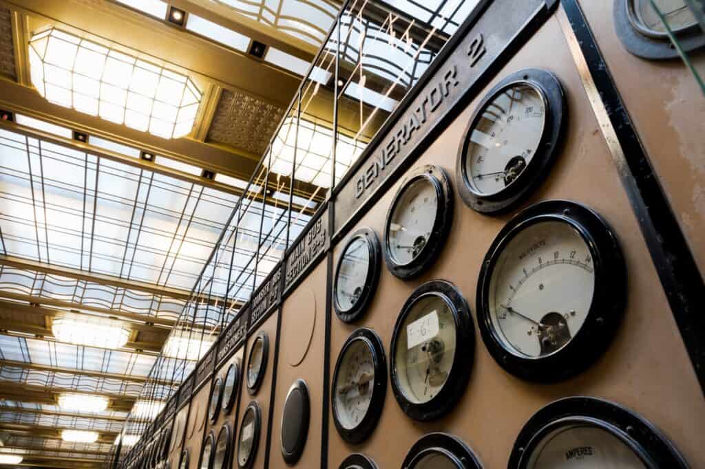 Close-up of large round meters on the Generator 2 switchboard in Control Room A at Battersea Power Station, the glowing coffered glass ceiling stretching away above