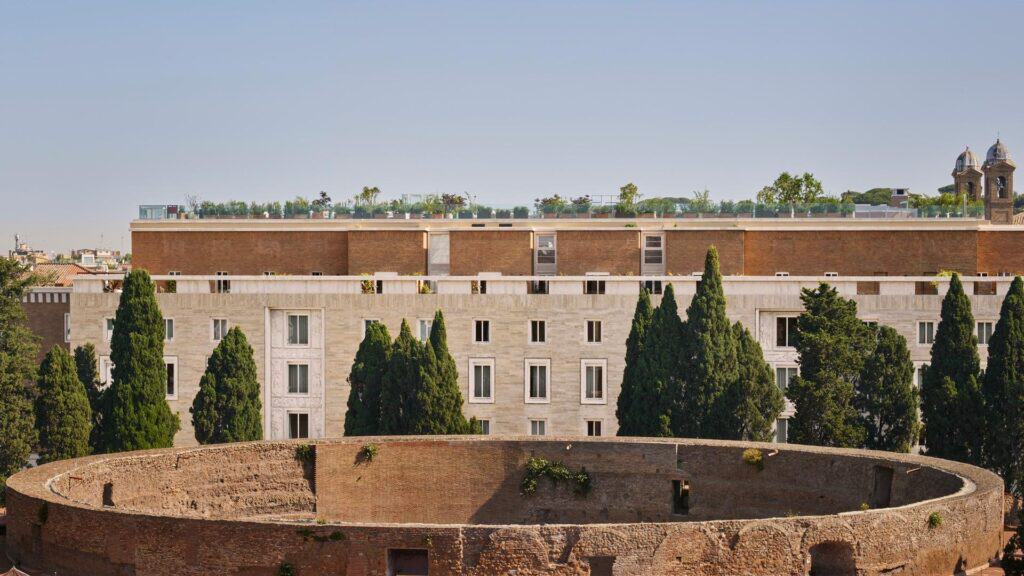 Bulgari Hotel Roma in Vittorio Ballio Morpurgo's 1930s brick and travertine building, seen behind the circular ruin of the Mausoleum of Augustus with cypress trees and a planted roof terrace on top
