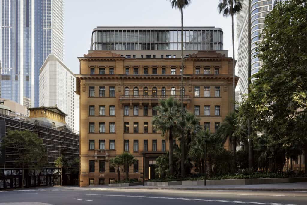 Restored Edwardian Baroque sandstone facade of Capella Sydney with palms and the set-back rooftop extension