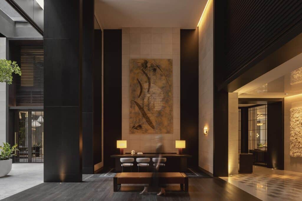 Dark-toned reception at Capella Sydney with stone wall, framed artwork and a timber desk