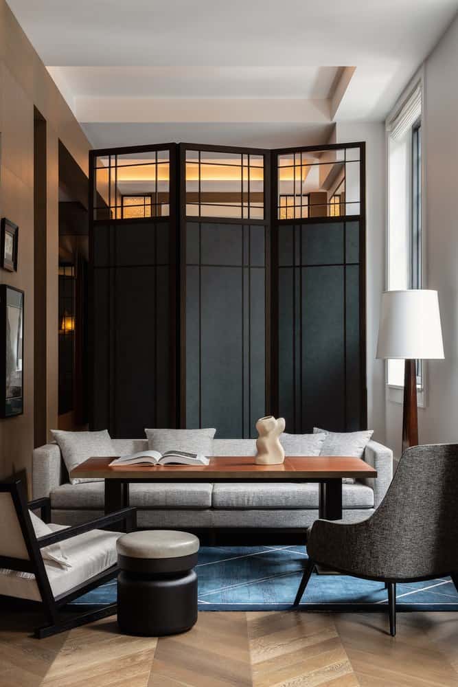 Guest room sitting area with grey sofa, black framed screen and herringbone timber floor at Capella Sydney