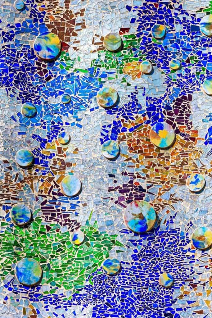 Close-up of the Casa Batlló facade covered in trencadís of broken glass and ceramic in cobalt, green, ochre and white, scattered with round polychrome ceramic discs