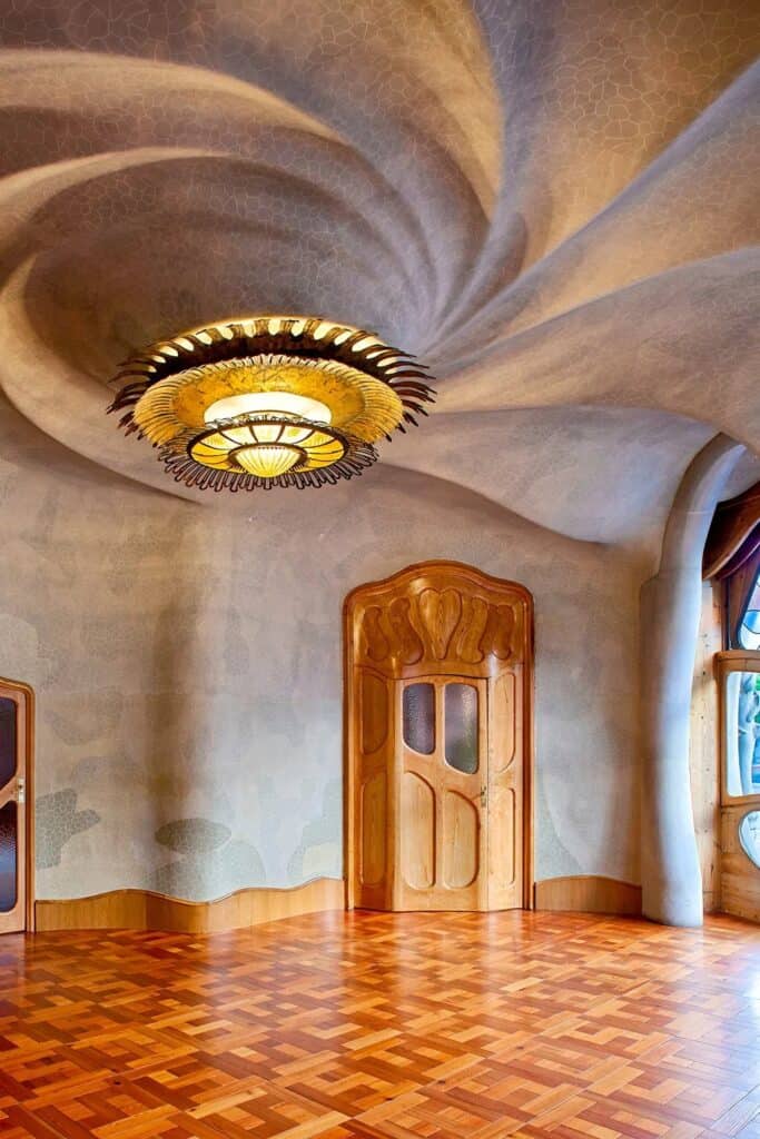 Whirlpool-shaped plaster ceiling of the Noble Floor salon at Casa Batlló swirling around a round gilded lamp, above a carved oak doorway and parquet floor