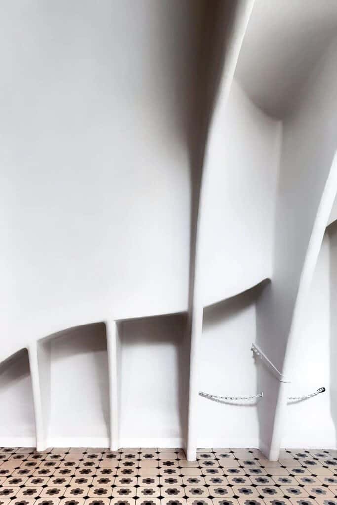 White catenary arches in the attic of Casa Batlló curving like the ribs of an animal above a black and white patterned tile floor