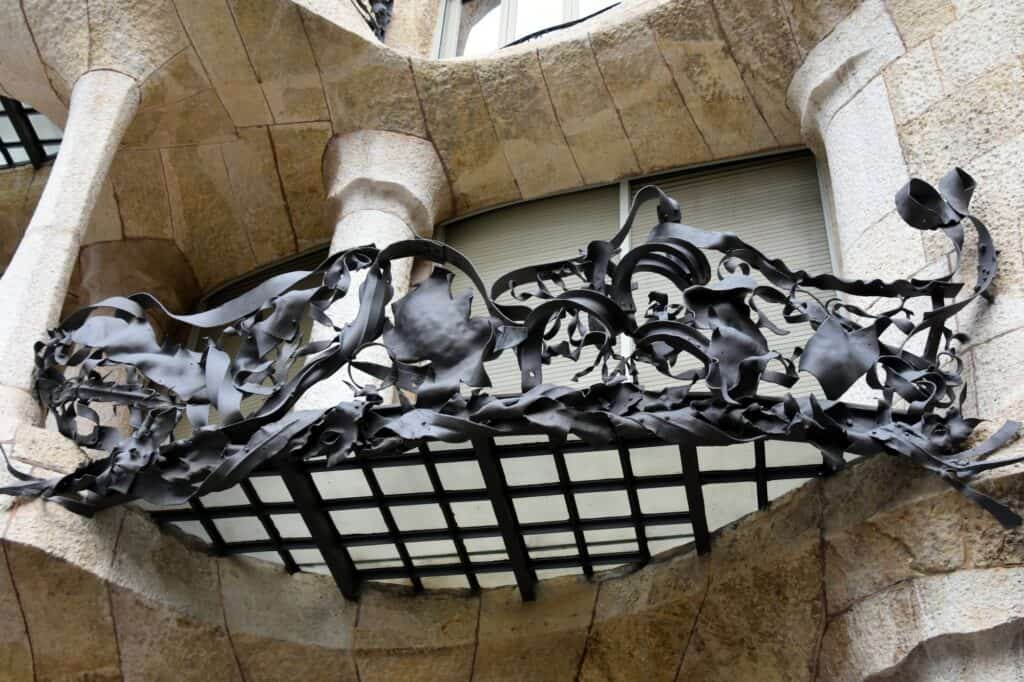 Close-up of a twisted wrought-iron balcony on Casa Milà, its seaweed-like black ironwork curling over a grid of glazing set into the soft curves of the carved limestone