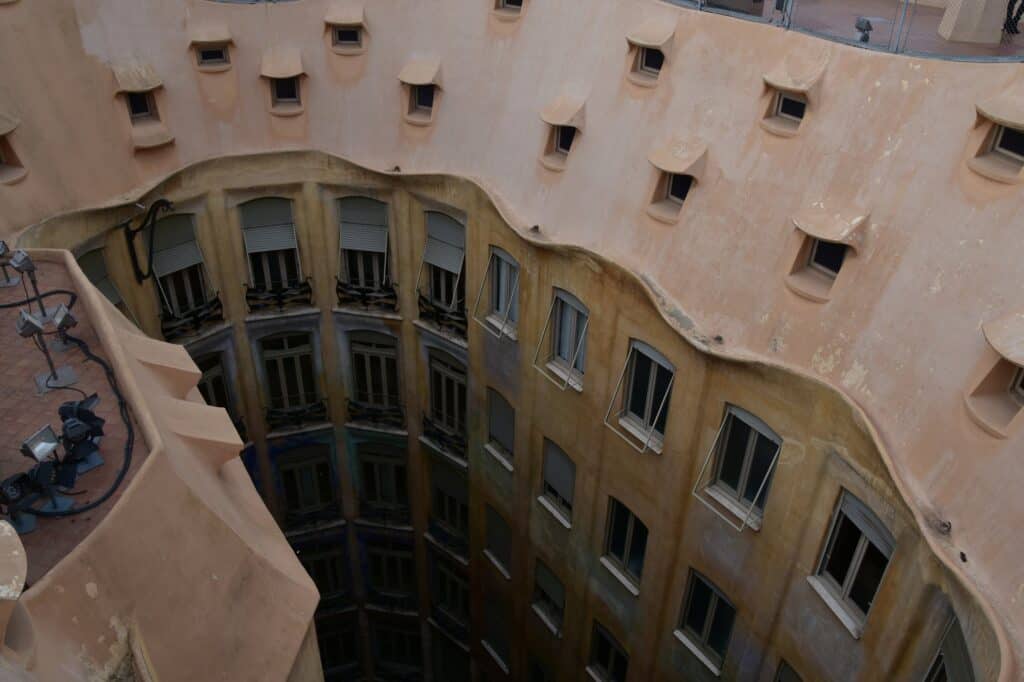 View from the roof of Casa Milà down into a courtyard, the cream rendered parapet pierced with small openings and the tiers of windows falling away below
