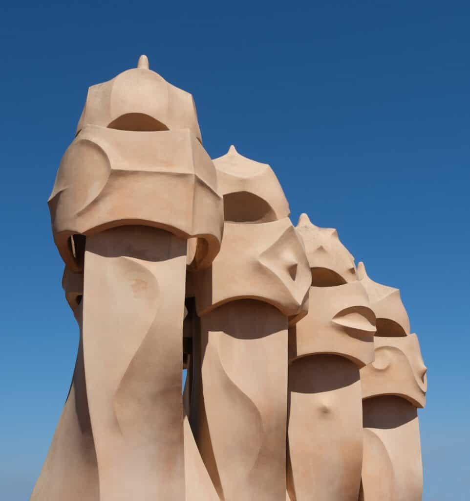 Group of helmet-like stone chimneys known as the warriors on the roof of Casa Milà, cream rendered masks set against a deep blue sky