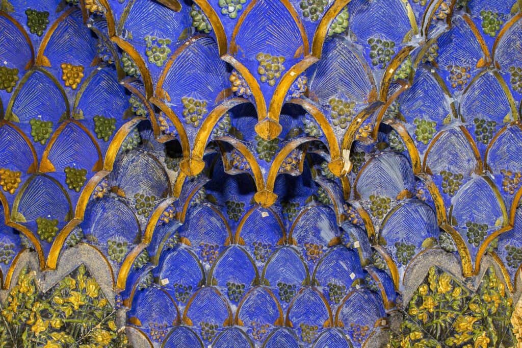 Close view of the restored smoking room ceiling at Casa Vicens, papier-mâché mocárabes in deep cobalt blue edged with gold ribs, hanging in honeycomb tiers above a frieze of yellow and green leaves