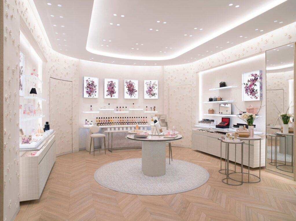 Oval accessories salon at Dior 30 Montaigne with a circular rug, a round central table, lacquered white display cabinets and framed pink floral prints on the cove-lit walls