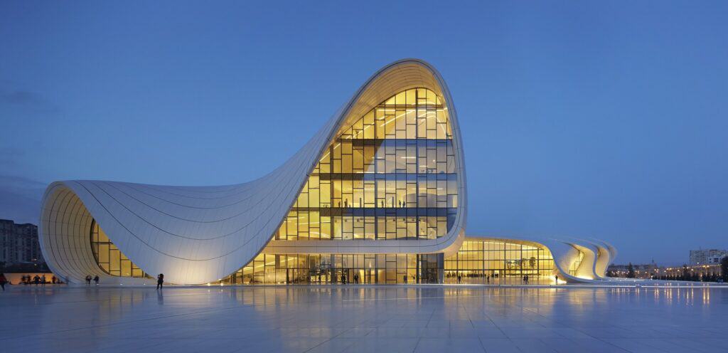 Glass curtain wall under the wave-like roof of the Heydar Aliyev Center at dusk