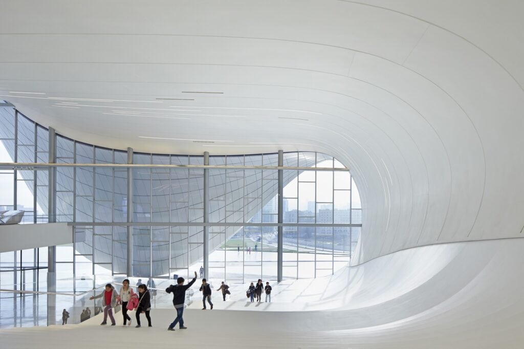 Visitors on a sloping white lobby floor beneath the undulating ceiling of the Heydar Aliyev Center