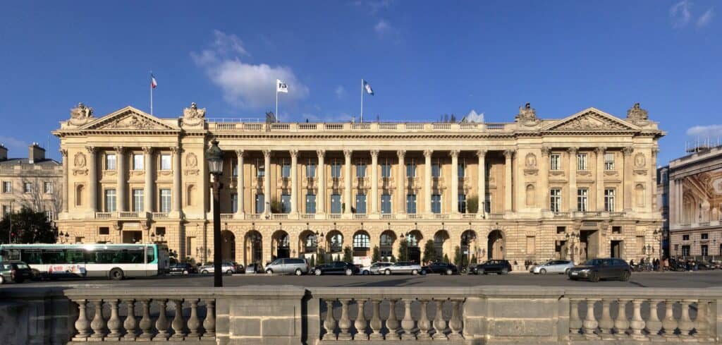 Hôtel de Crillon on Place de la Concorde in Paris, Ange-Jacques Gabriel's long limestone façade with a Corinthian colonnade above arcades, end pediments and flags on the roof under a blue sky