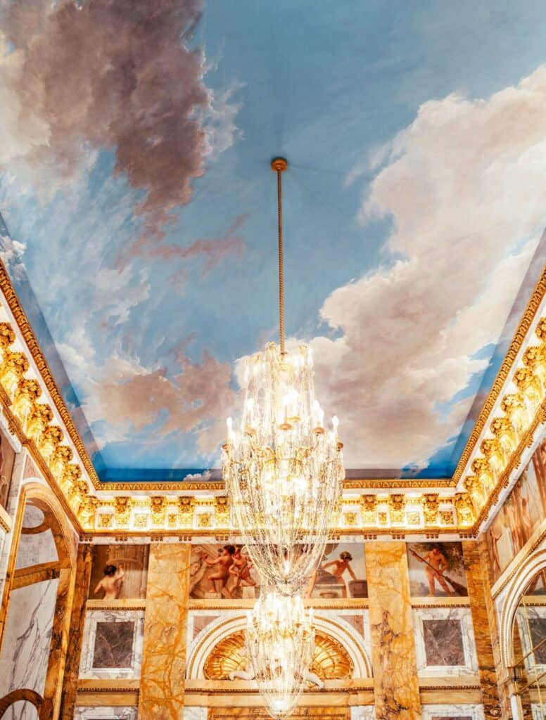 Les Ambassadeurs bar at Hôtel de Crillon, a painted sky of clouds on the landmarked ceiling above a gilded cornice, a tall crystal chandelier and walls of gilt-framed coloured marble panels
