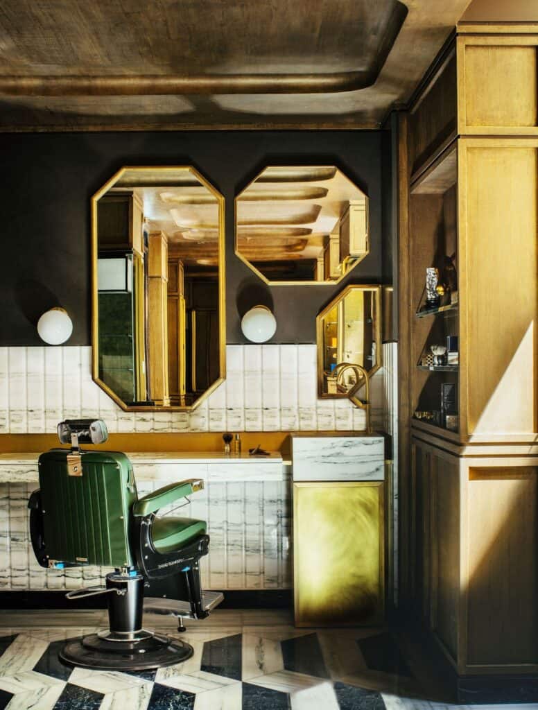 Men's grooming salon at Hôtel de Crillon, a green leather barber's chair before octagonal brass mirrors on a dark wall, white tiles, oak panelling and a zigzag black and white marble floor