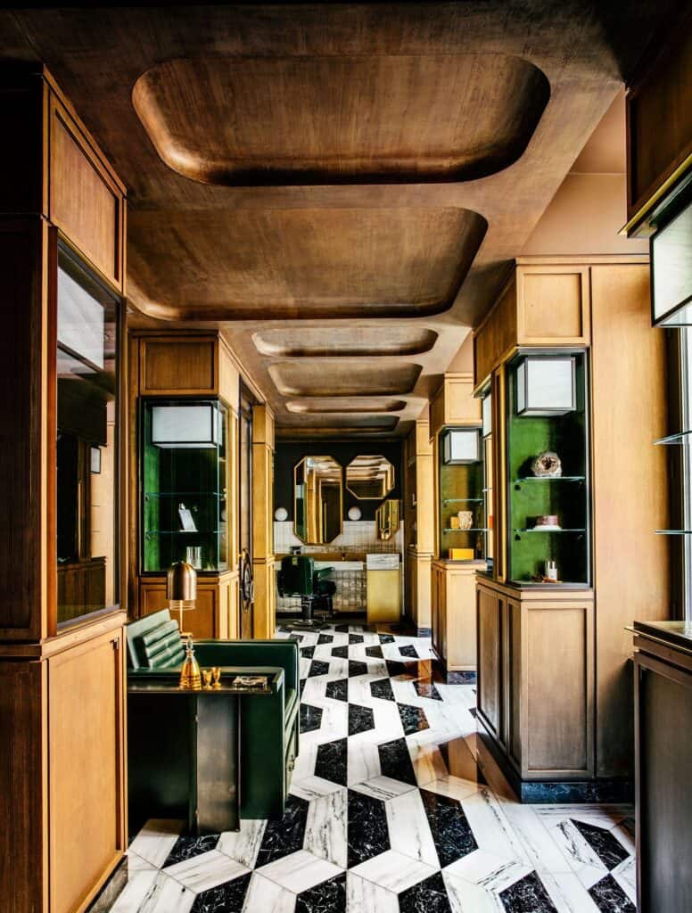 Corridor of the grooming salon at Hôtel de Crillon lined with oak panelling and green-lit display niches under a coffered bronze ceiling, on a zigzag floor of black and white marble