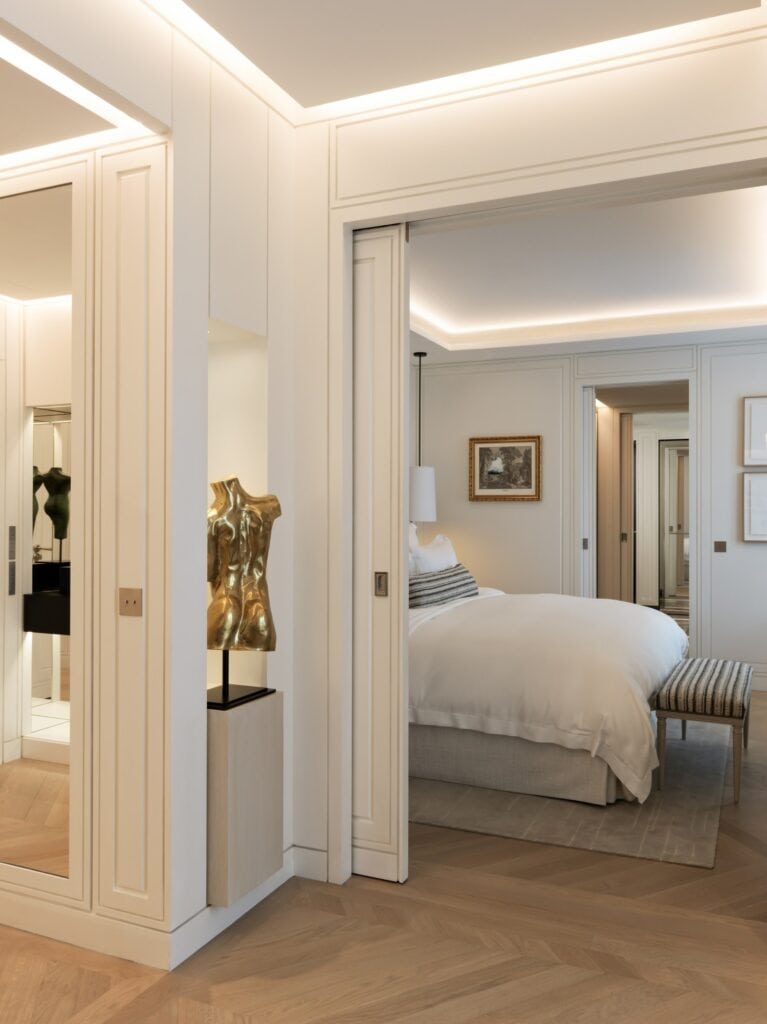 Jardin suite at Hôtel de Crillon designed by Aline Asmar d'Amman, a gilded torso sculpture on a plinth in the white panelled entry and a bedroom beyond on a herringbone oak floor