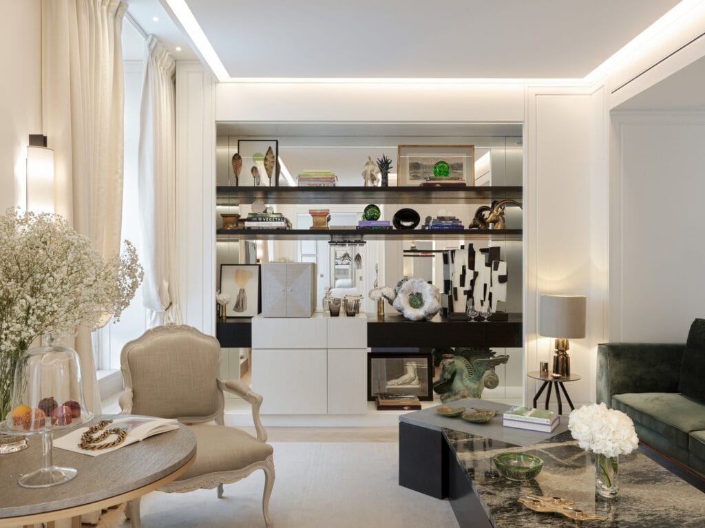 Living room of a Jardin suite at Hôtel de Crillon with black lacquered shelves of art books and objects, a Louis-style armchair, a green velvet sofa and white hydrangeas