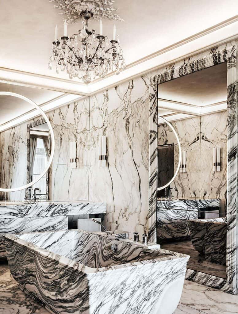 Marble bathroom at Hôtel de Crillon with a sculpted bath of black-veined white marble, matching marble walls, round mirrors and a crystal chandelier