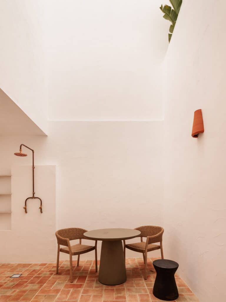 Private patio of a Medina room at Hotel Palácio de Tavira, a copper outdoor shower and a small round table with two chairs on terracotta tiles between tall whitewashed walls open to the sky