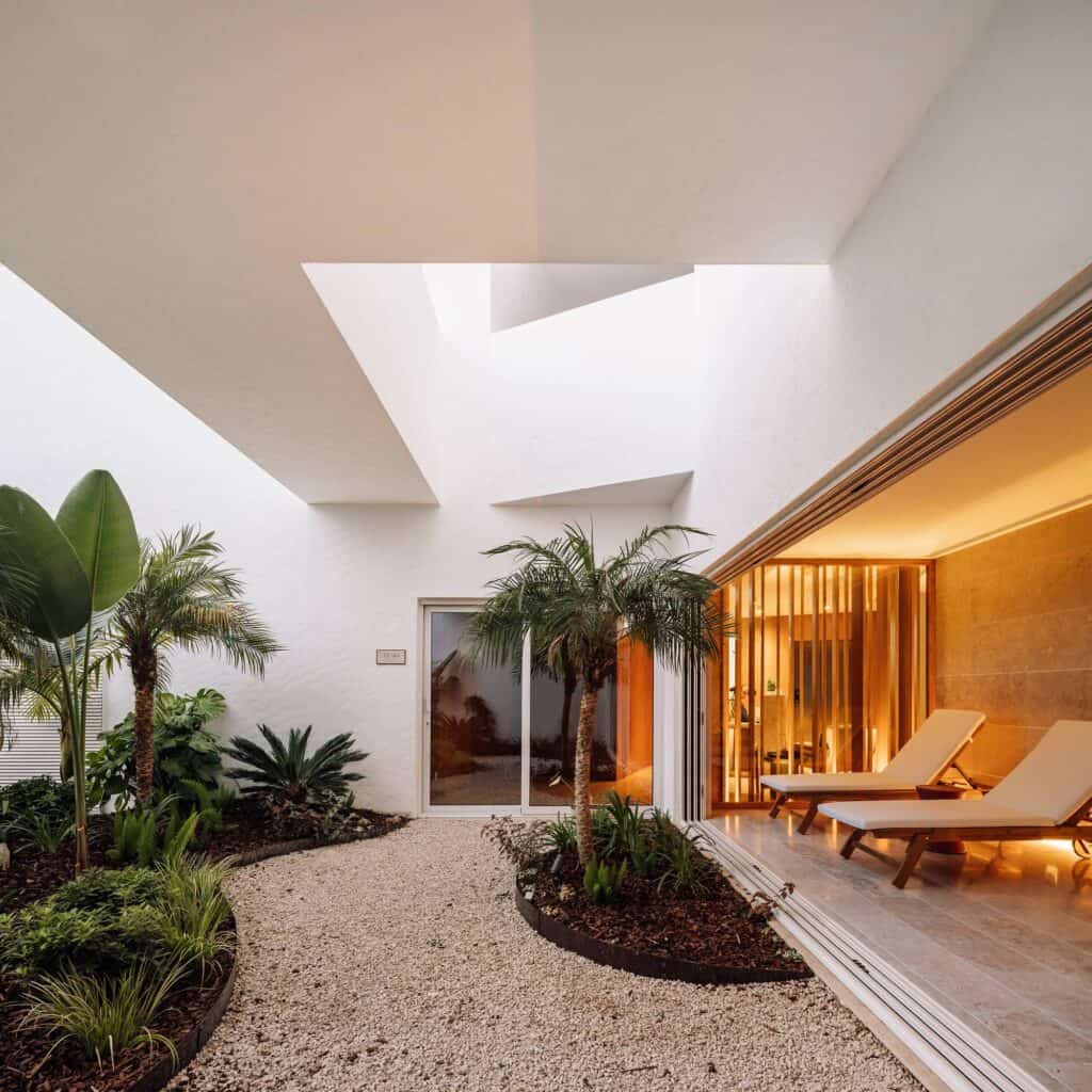 Planted patio at Hotel Palácio de Tavira, palms and gravel between white walls beside a timber-lined room with sun loungers behind sliding glass doors, under a framed opening to the sky