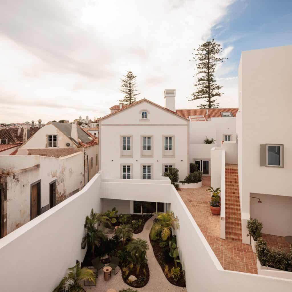 Sunken garden in the Medina at Hotel Palácio de Tavira, tropical planting between white walls with a terracotta-tiled stair, looking to a white gabled house and tall pines