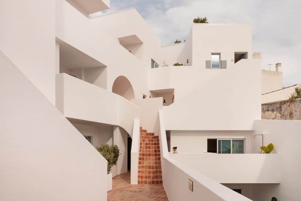 Medina wing of Hotel Palácio de Tavira, a cluster of white cubic volumes with arches, terraces and parapets around a narrow terracotta-tiled stair