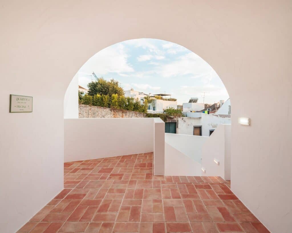 Roof terrace in the Medina at Hotel Palácio de Tavira, a round-arched opening in a white wall framing the rooftops of Tavira above a terracotta-tiled floor
