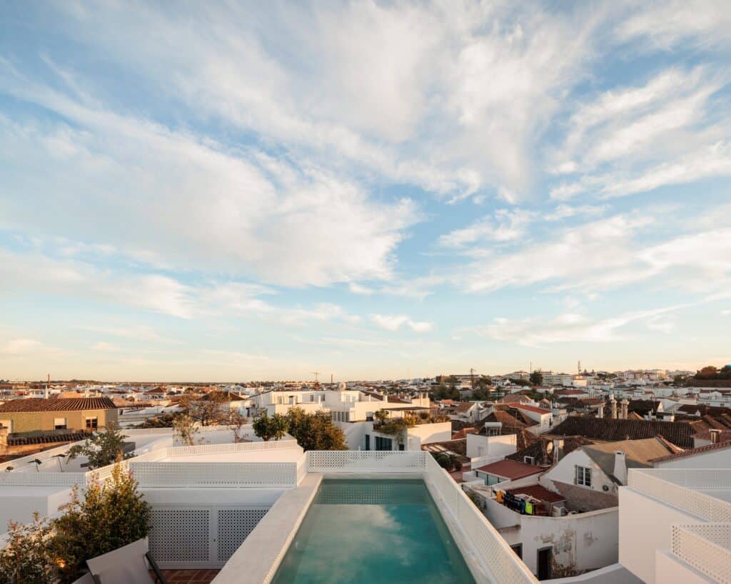 Rooftop pool at Hotel Palácio de Tavira, a narrow turquoise pool set between white parapets above the tiled roofs of Tavira under a wide evening sky