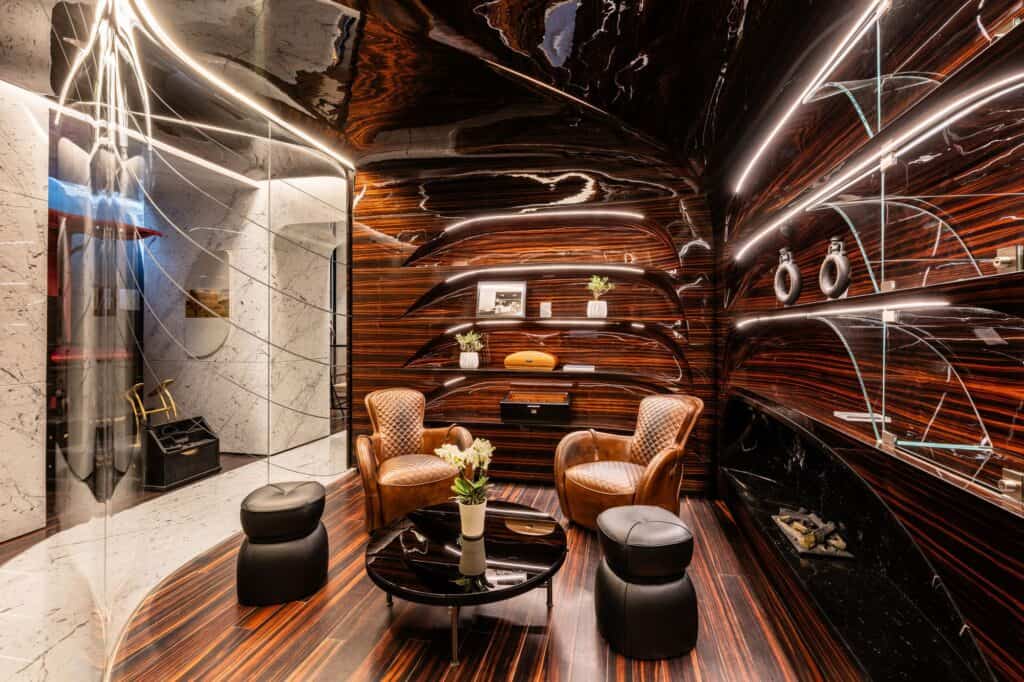 Cigar lounge at Hotel Romeo Roma wrapped in polished Makassar ebony with curving shelves, glass display fins, two leather armchairs and a white marble wall