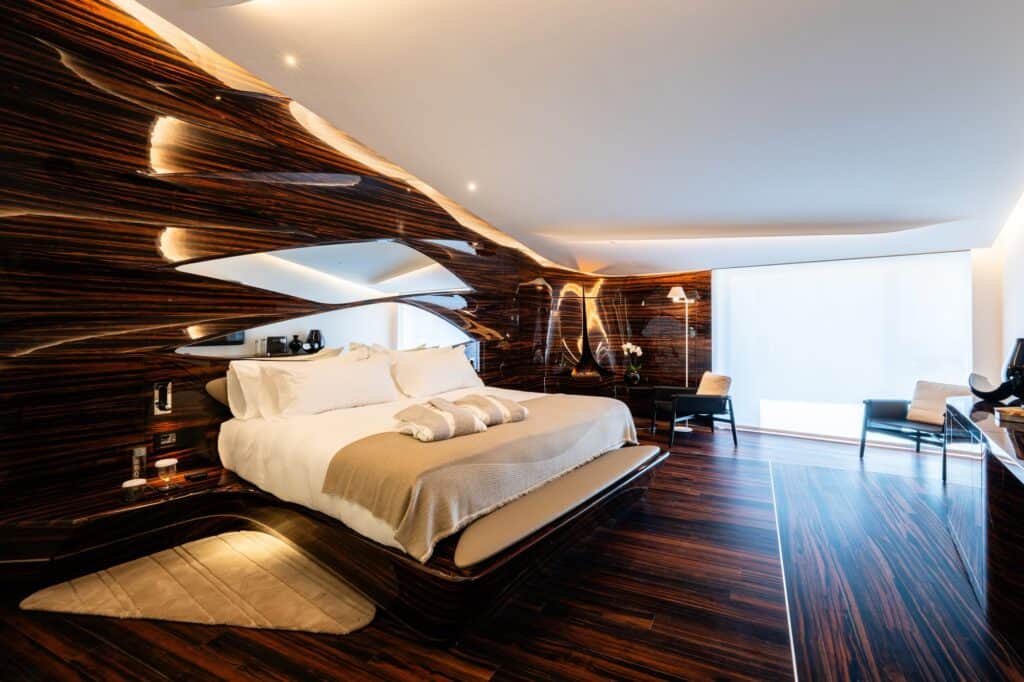 Hotel Romeo Roma guest room with sculpted Makassar ebony walls that swell and fold around the bed, a white ceiling and a pale rug on the dark striped floor