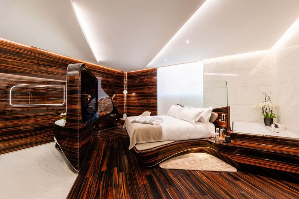 Grand Suite at Hotel Romeo Roma with a curved ebony headboard partition, a bed on a flowing timber plinth, a white marble bath area and long glowing cove lights