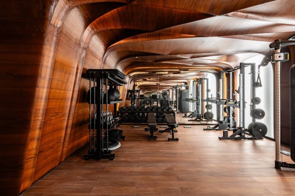 Fitness centre at Hotel Romeo Roma clad in warm timber that rolls overhead in undulating vaults above rows of black gym equipment