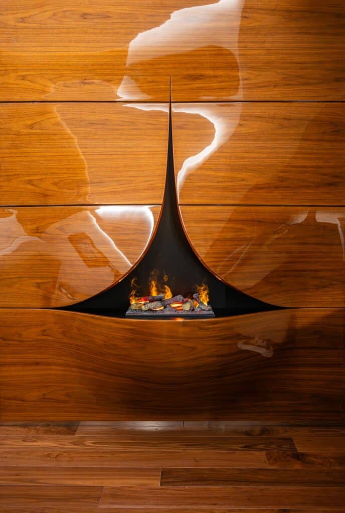 Black teardrop-shaped fireplace suspended in a glossy walnut wall of a Hotel Romeo Roma guest room, flames glowing in its opening above the wooden floor