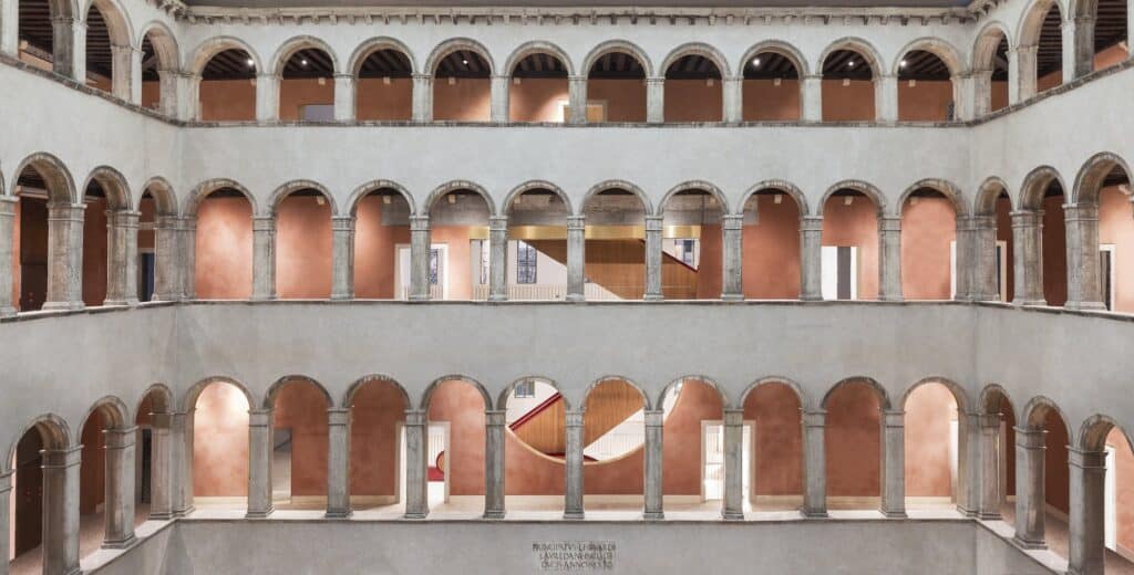 Symmetrical view across the courtyard of Il Fondaco dei Tedeschi, tiers of stone arcades with round arches and slender columns opening onto warm terracotta-coloured loggia walls