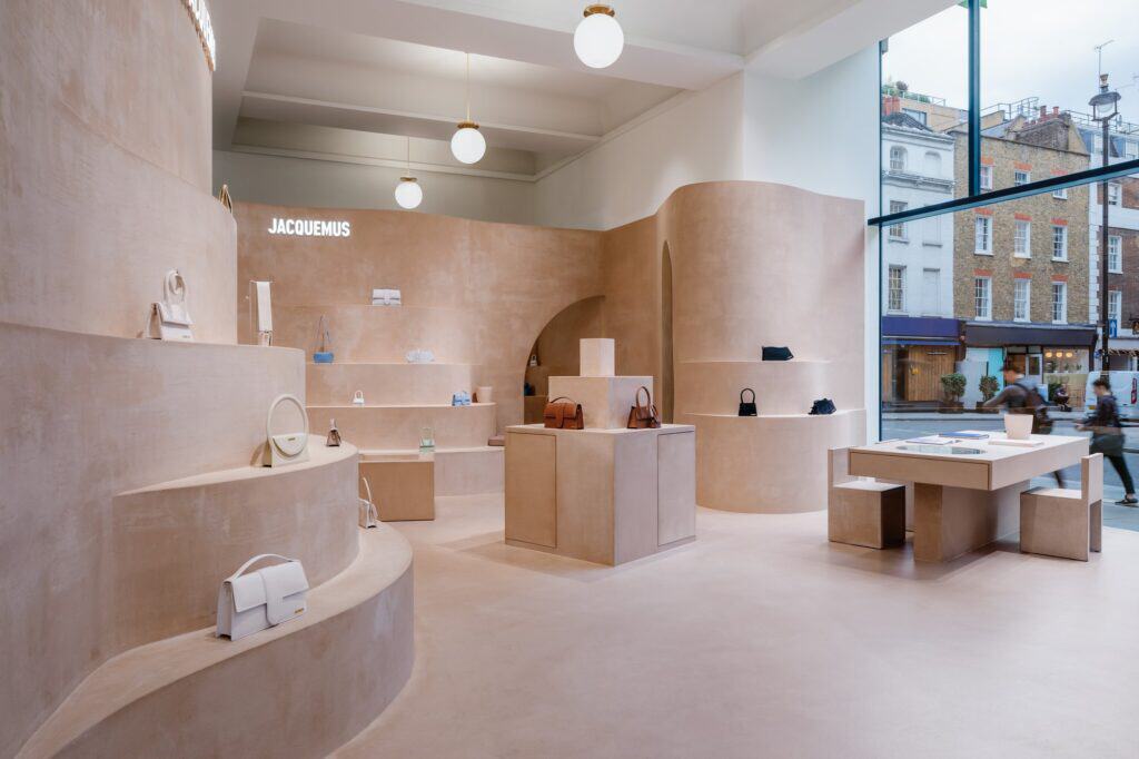 Wide view of Jacquemus Store Selfridges London with tiered clay shelving, a central plinth and a table by the street window