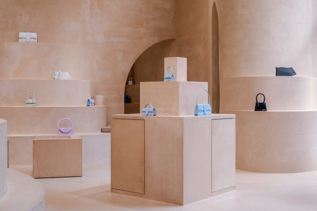 Stacked terracruda plinths with pale blue Jacquemus bags before stepped curved shelves and a tall arched doorway at Selfridges London