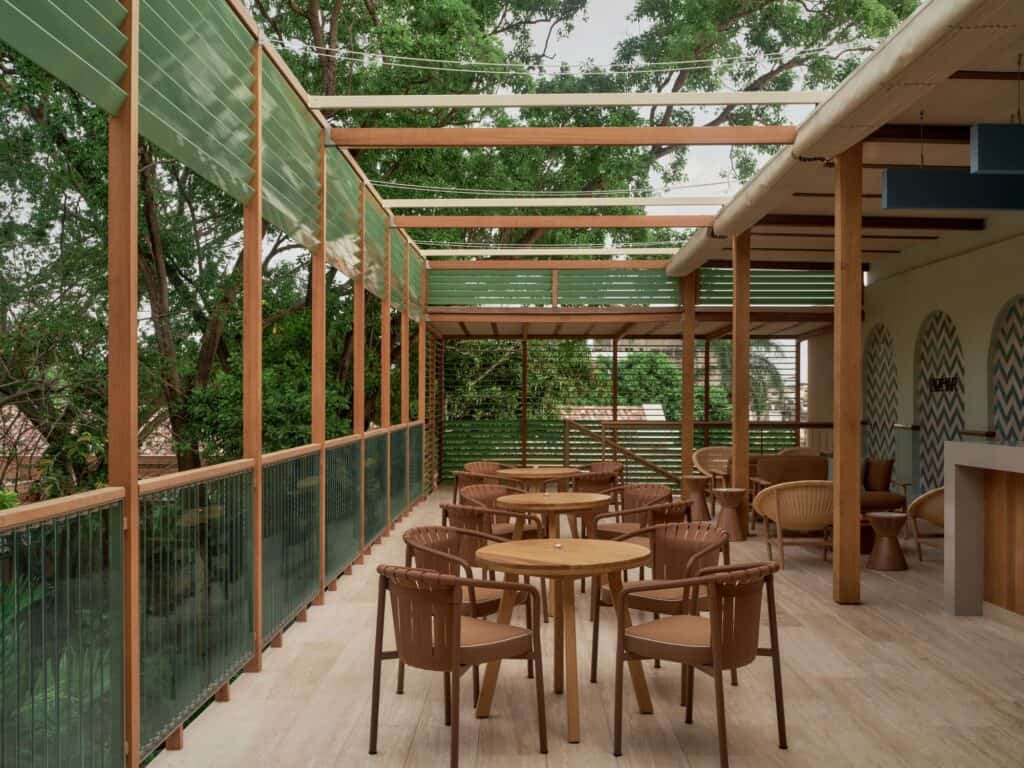 Covered restaurant terrace at Kimpton Las Mercedes Hotel, slender timber posts and a green slatted pergola over wooden tables and chairs, with patterned tile panels on the wall