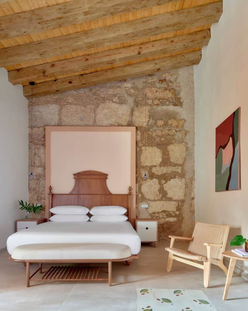 Guest room at Kimpton Las Mercedes Hotel in the colonial building, a carved timber headboard against an exposed coral-stone wall beneath old timber ceiling beams