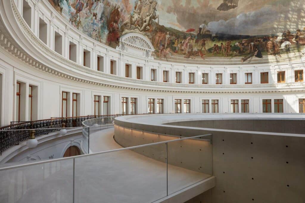 Curved concrete walkway and glass balustrade overlooking the painted panorama at La Bourse de Commerce