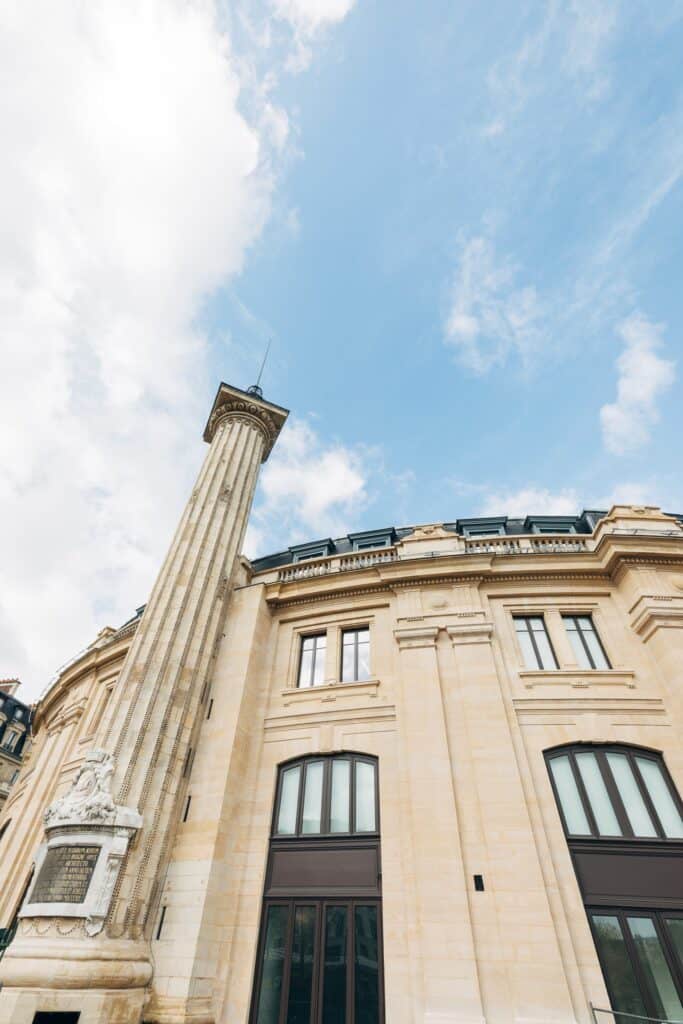 Stone corner of La Bourse de Commerce with ornate column and tall windows, Paris